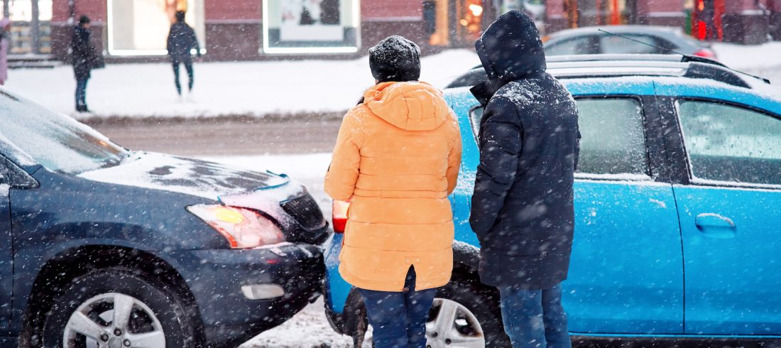 Drivers look at damaged cars after road accident in blizzard. Car crash accident on winter road with snow, unsafe distance when driving on slippery roads. Winter driving – car breakdown Winter driving car accident on Thanksgiving Weekend.